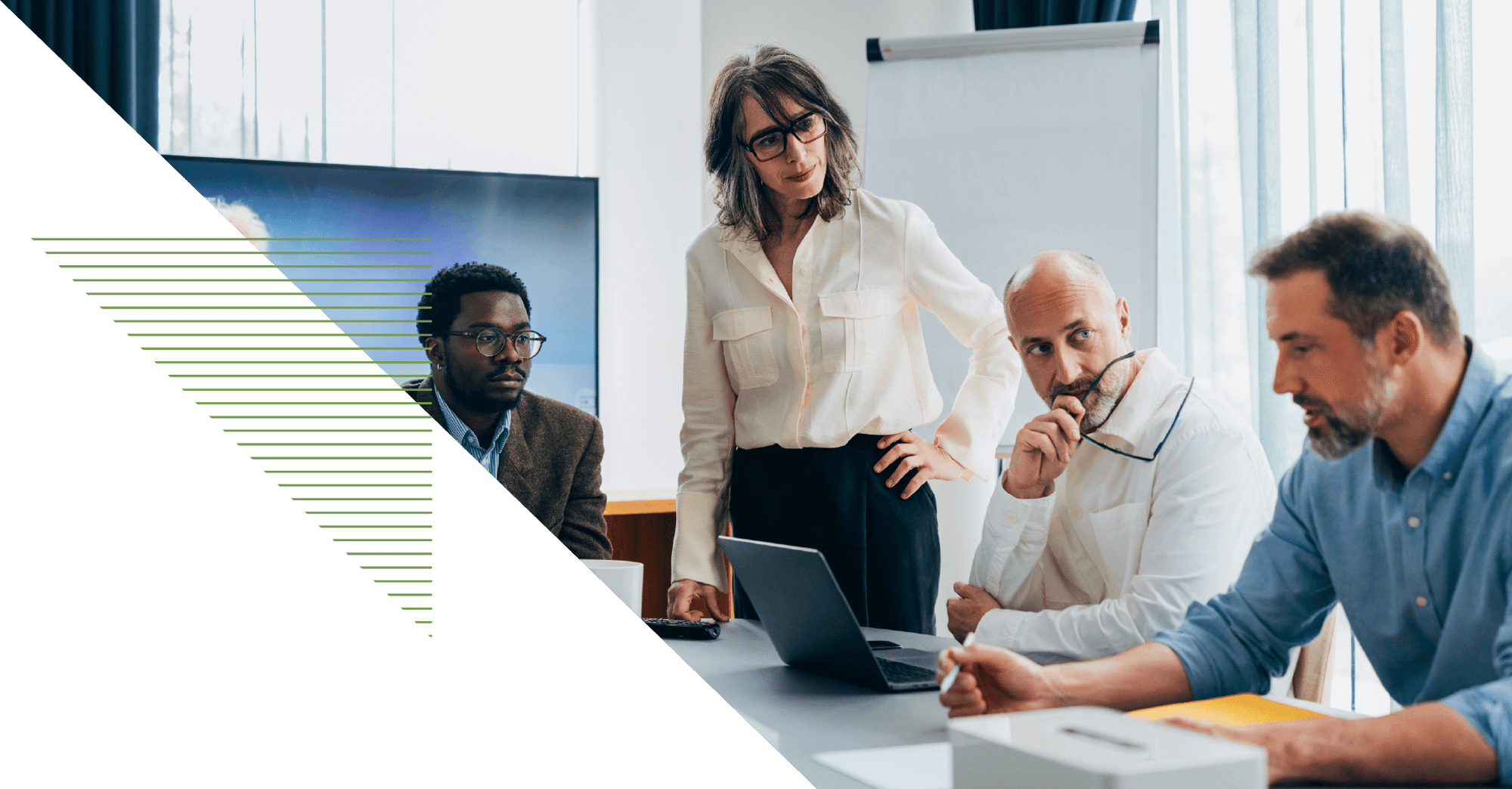 four business people sit together at a conference table, one stands with their hand on their hip deep in discussion four business people sit together at a conference table, one stands with their hand on their hip deep in discussion